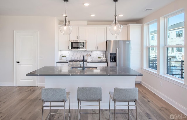 kitchen with decorative backsplash, appliances with stainless steel finishes, a center island with sink, and white cabinets