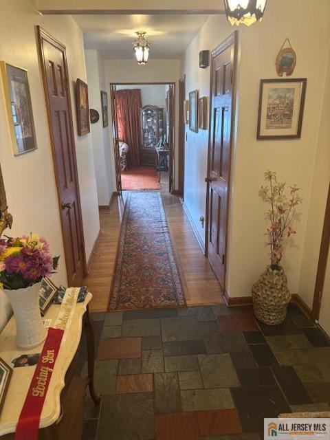 corridor featuring stone finish floor, a notable chandelier, and baseboards