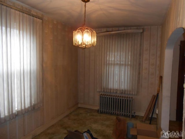 unfurnished dining area featuring wood walls, radiator, an inviting chandelier, and lofted ceiling