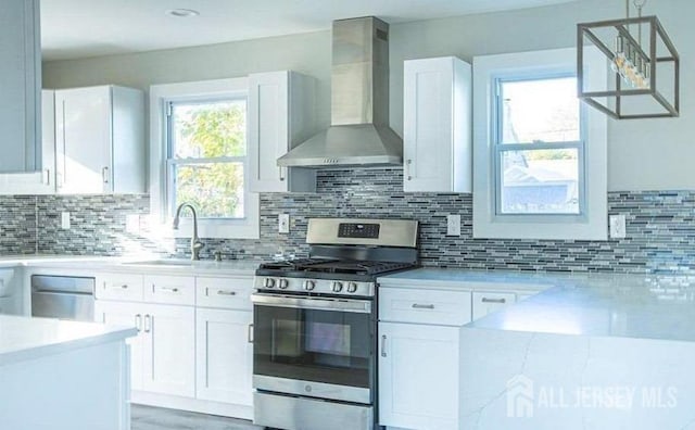 kitchen with tasteful backsplash, appliances with stainless steel finishes, white cabinets, wall chimney exhaust hood, and pendant lighting