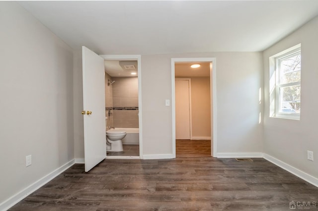 unfurnished bedroom featuring dark wood-style floors, visible vents, baseboards, and ensuite bathroom