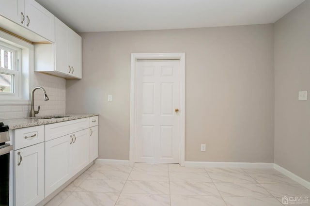 kitchen with light stone counters, marble finish floor, tasteful backsplash, white cabinets, and a sink