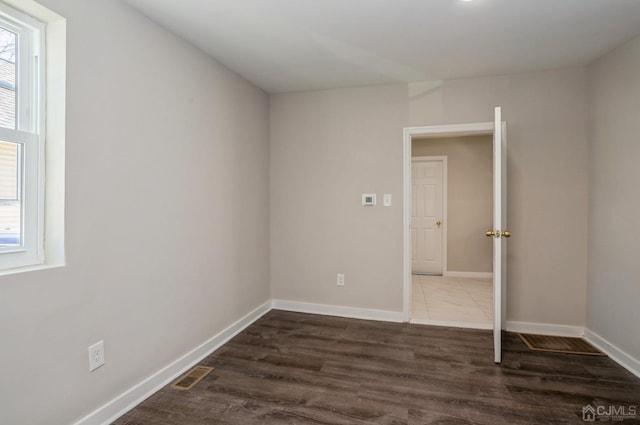 unfurnished bedroom featuring dark wood-style flooring, visible vents, baseboards, and multiple windows