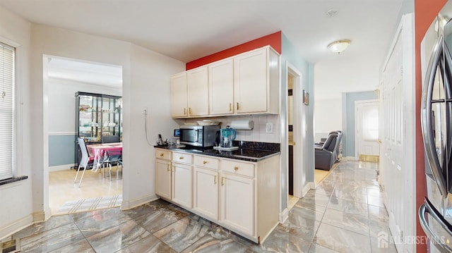 kitchen with tasteful backsplash, dark stone counters, appliances with stainless steel finishes, marble finish floor, and white cabinetry