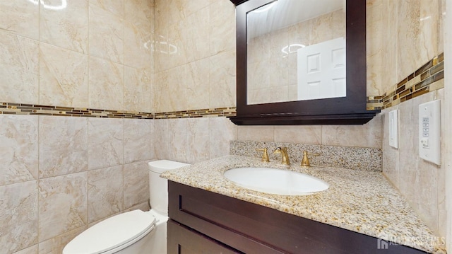 bathroom featuring decorative backsplash, tile walls, vanity, and toilet