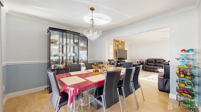 dining space featuring ornamental molding, light wood finished floors, a notable chandelier, and baseboards