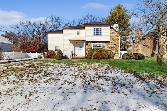 view of front facade featuring entry steps, a lawn, stone siding, a chimney, and fence