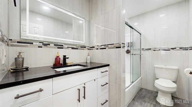 full bathroom featuring toilet, vanity, tile walls, combined bath / shower with glass door, and tile patterned floors