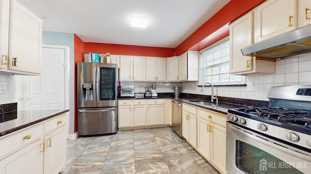 kitchen featuring appliances with stainless steel finishes, dark stone countertops, a sink, and under cabinet range hood