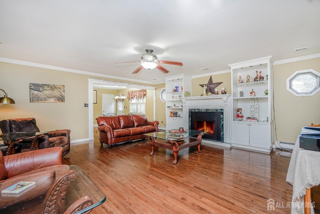 living room with wood finished floors, visible vents, a lit fireplace, ornamental molding, and baseboard heating