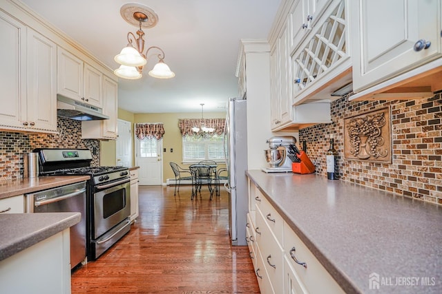 kitchen with decorative backsplash, appliances with stainless steel finishes, wood finished floors, under cabinet range hood, and a chandelier