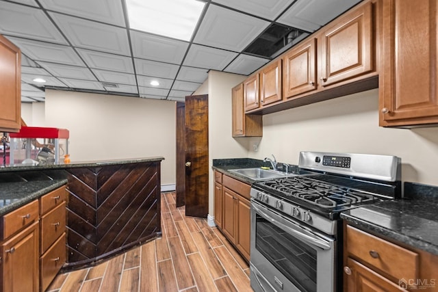 kitchen with sink, stainless steel gas range, baseboard heating, and dark stone counters