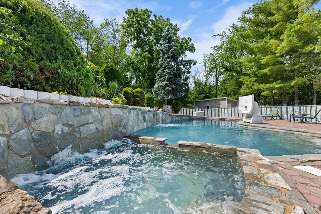 view of pool with fence and a pool with connected hot tub