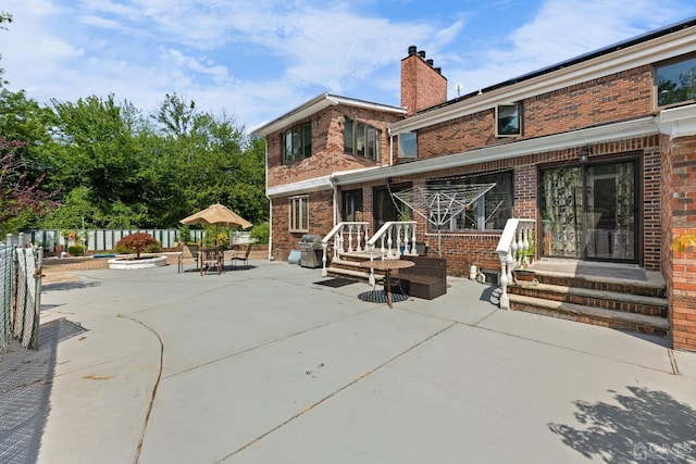 back of property featuring fence, brick siding, a chimney, and a patio area