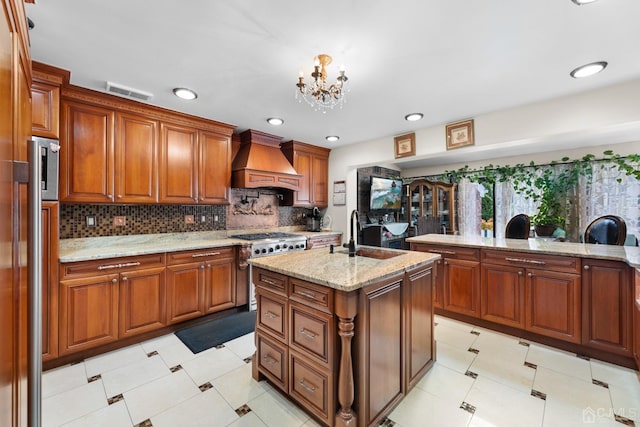 kitchen featuring premium range hood, an island with sink, sink, range, and light stone countertops