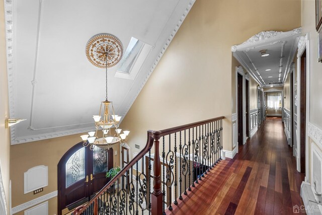 corridor with an upstairs landing, high vaulted ceiling, hardwood / wood-style floors, an inviting chandelier, and stairs