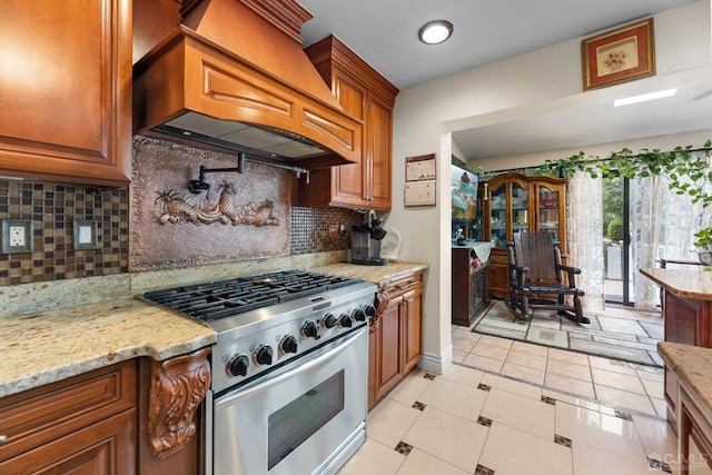 kitchen with light tile patterned floors, premium range hood, stainless steel range with gas stovetop, light stone countertops, and decorative backsplash