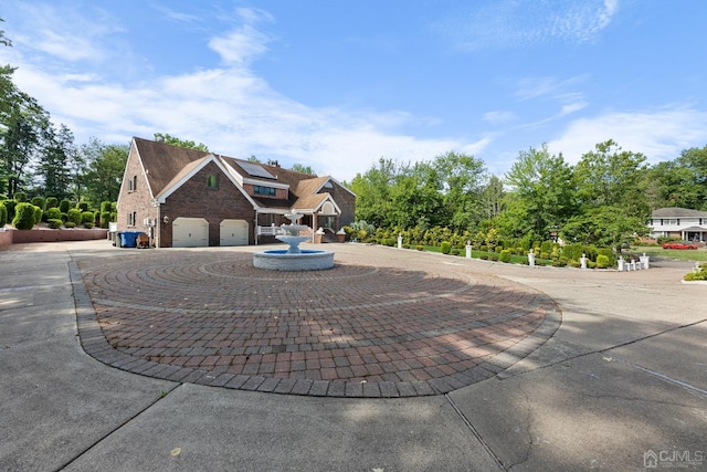 view of front of home with brick siding, roof mounted solar panels, curved driveway, and an attached garage