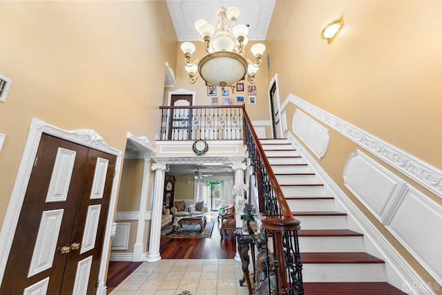 entrance foyer featuring stairway, a high ceiling, light tile patterned floors, decorative columns, and a chandelier