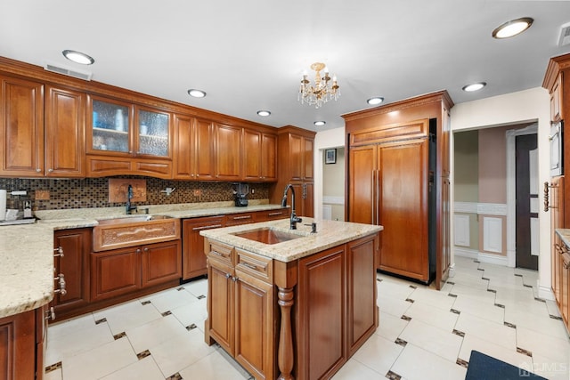 kitchen with light stone countertops, sink, a center island with sink, and paneled built in refrigerator