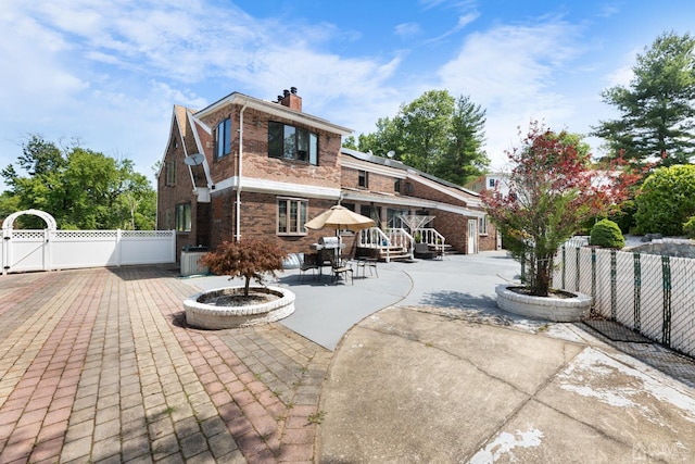 back of house with a gate, fence, brick siding, and a chimney