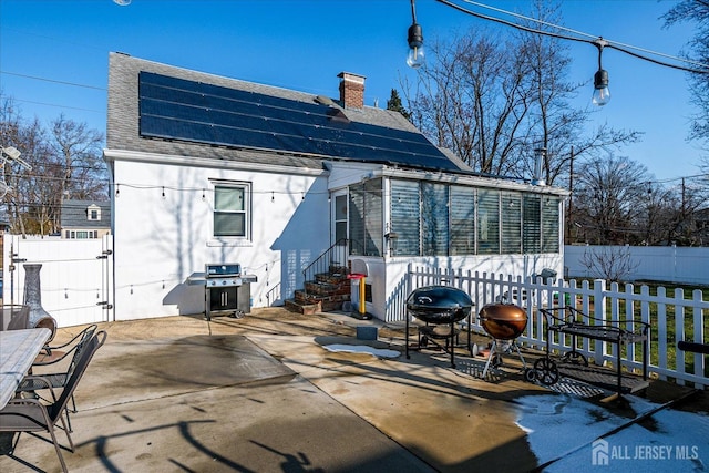 rear view of house with a sunroom, a patio area, and solar panels