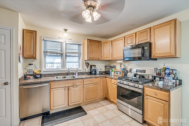 kitchen featuring sink, light tile patterned floors, ceiling fan, appliances with stainless steel finishes, and dark stone counters