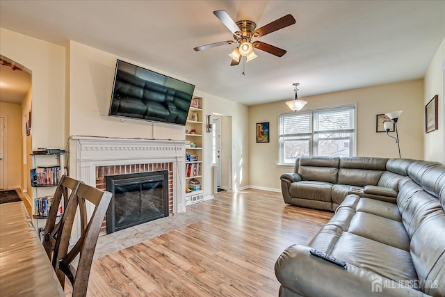 living room with ceiling fan, a brick fireplace, and light hardwood / wood-style floors