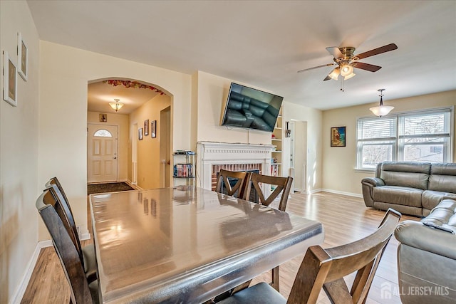 dining space featuring a fireplace, ceiling fan, and light wood-type flooring