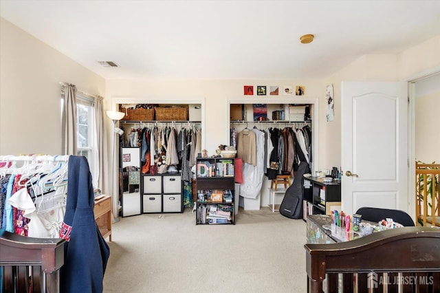 bedroom featuring visible vents, light carpet, and two closets