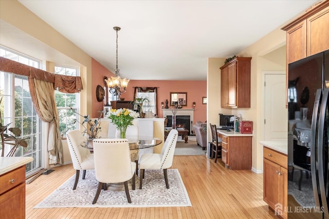 dining area featuring a lit fireplace, a notable chandelier, and light wood-style flooring