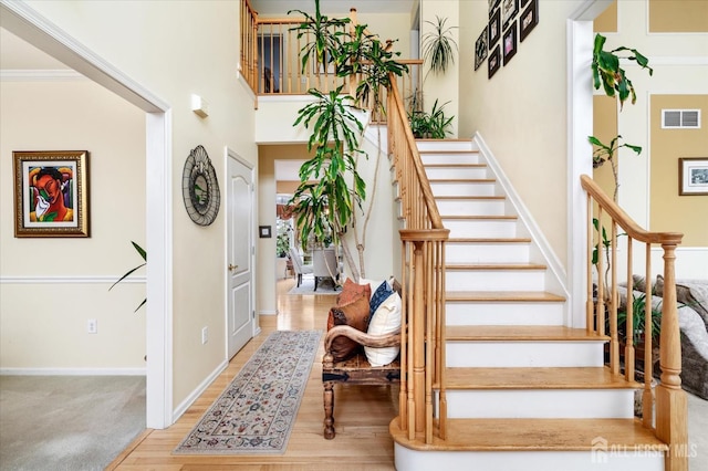 staircase with wood finished floors, a towering ceiling, visible vents, and baseboards