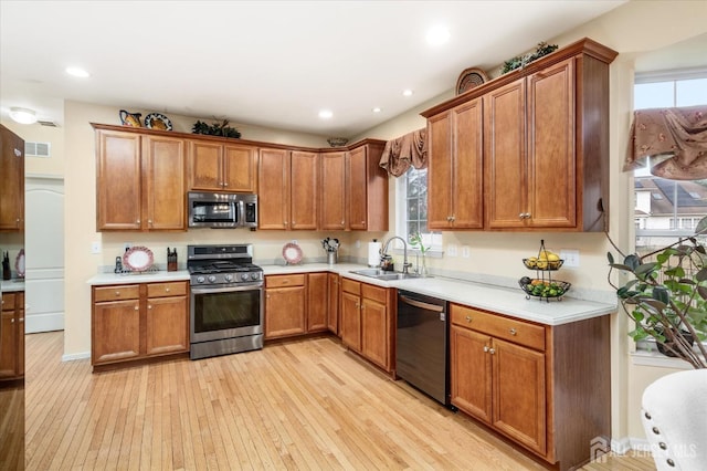 kitchen featuring stainless steel appliances, light countertops, light wood-style flooring, brown cabinetry, and a sink