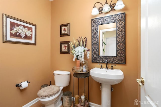 half bathroom with a chandelier, a sink, toilet, and baseboards