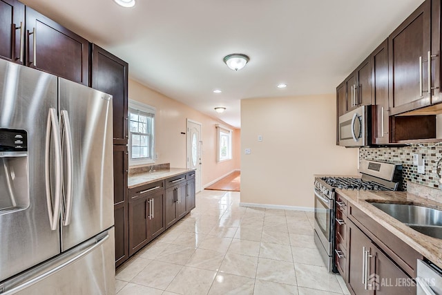 kitchen with appliances with stainless steel finishes, dark brown cabinetry, baseboards, light stone counters, and recessed lighting