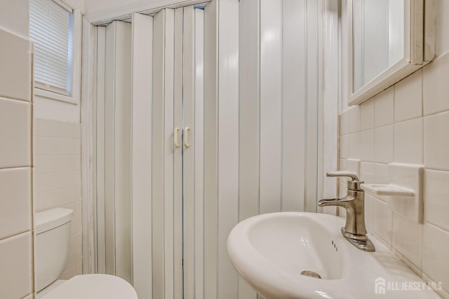 half bath with a sink, tile walls, and toilet