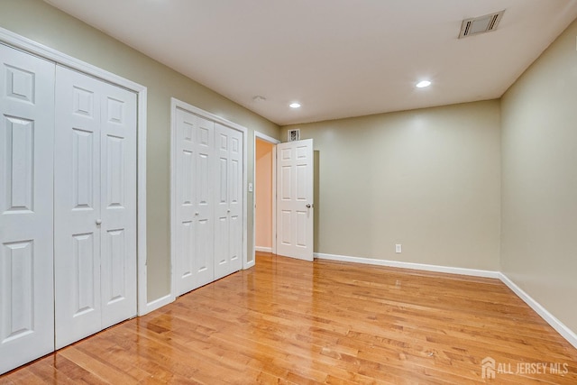 unfurnished bedroom with two closets, light wood finished floors, baseboards, and recessed lighting