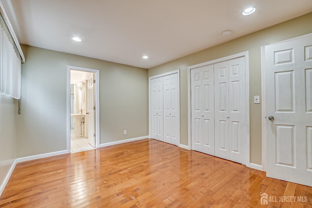 unfurnished bedroom with multiple closets, baseboards, light wood-style flooring, recessed lighting, and connected bathroom