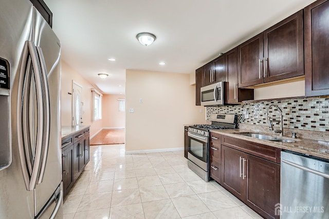kitchen featuring stainless steel appliances, a sink, decorative backsplash, dark brown cabinets, and light stone countertops
