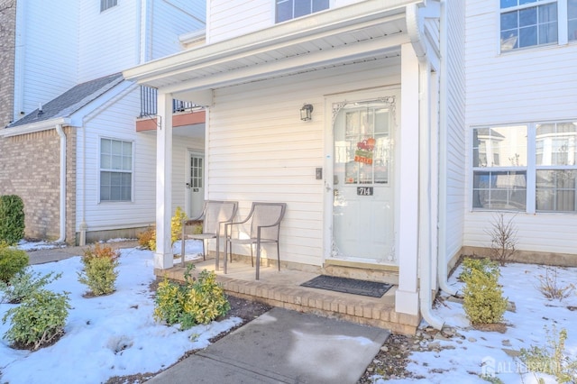 snow covered property entrance with a porch and brick siding