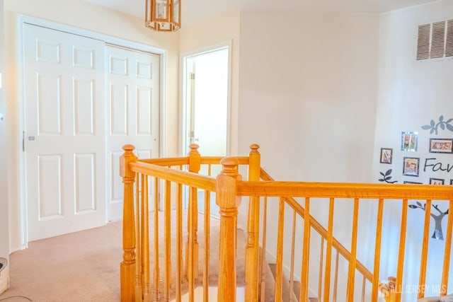 hall with visible vents, light colored carpet, and an upstairs landing