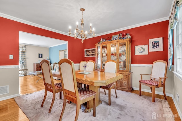 dining area featuring crown molding, a notable chandelier, and light hardwood / wood-style flooring