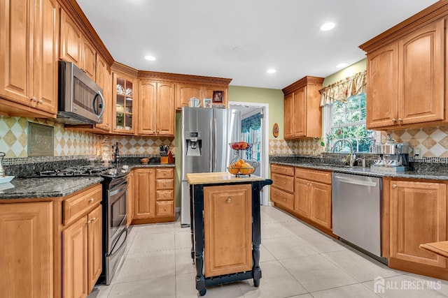 kitchen with appliances with stainless steel finishes, sink, dark stone counters, a center island, and light tile patterned floors