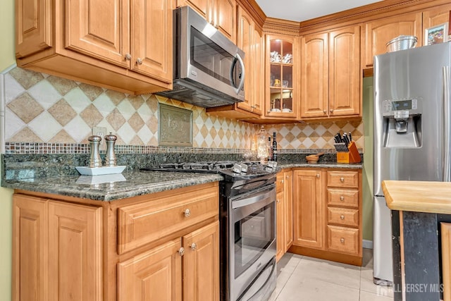 kitchen featuring appliances with stainless steel finishes, light tile patterned floors, decorative backsplash, and dark stone countertops