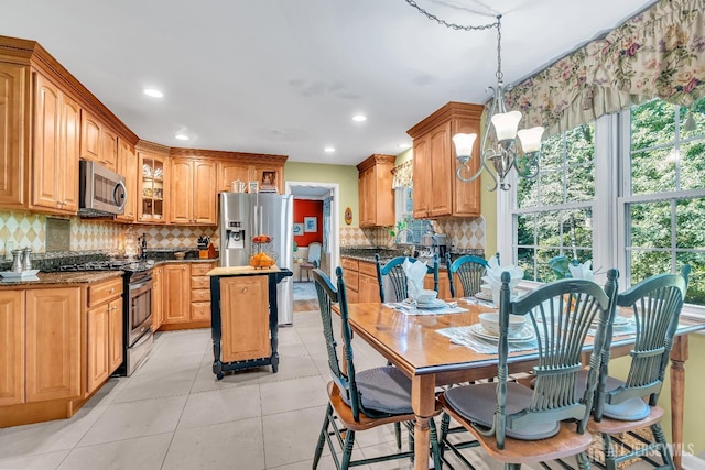 kitchen with light tile patterned flooring, hanging light fixtures, appliances with stainless steel finishes, a kitchen island, and backsplash