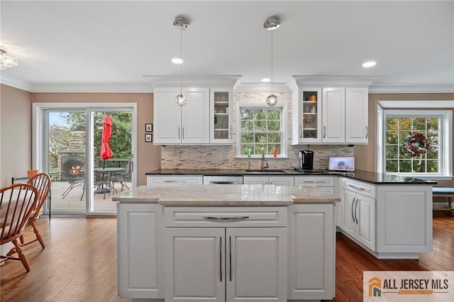 kitchen featuring a sink, dark wood-type flooring, a kitchen island, healthy amount of natural light, and crown molding