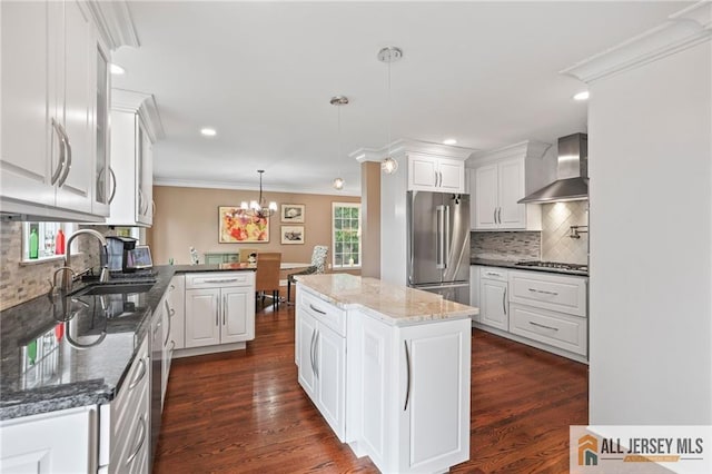 kitchen featuring wall chimney exhaust hood, stainless steel appliances, a sink, tasteful backsplash, and white cabinetry
