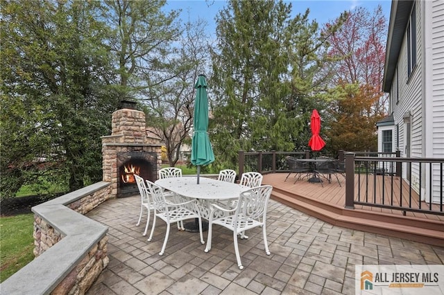 view of patio / terrace with outdoor dining space, a deck, an outdoor stone fireplace, and view of wooded area