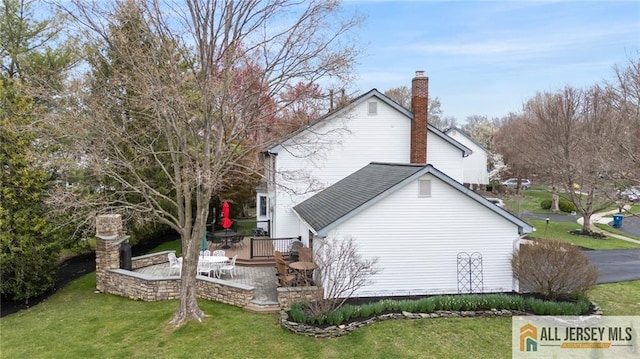 view of side of home with a yard, a chimney, and a deck