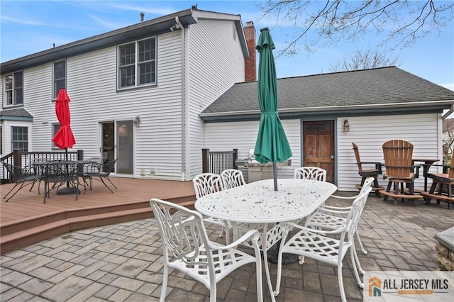 rear view of property with outdoor dining area, a deck, a patio area, and a chimney